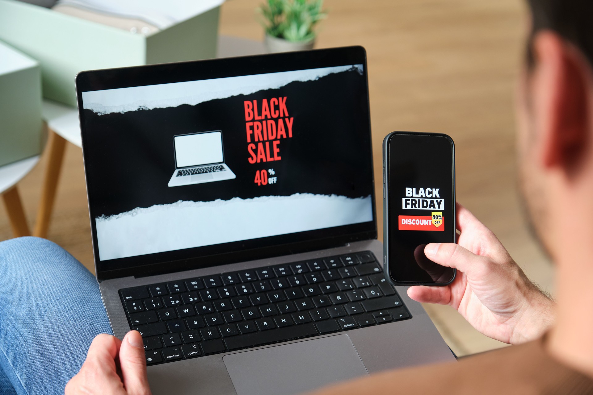 Man is comparing black friday deals on laptop and smartphone at home